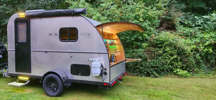 Teardrop RV rental parked in lush greenery, showing its open rear galley kitchen and side features.. Bend Teardrop Tall Boy 2023