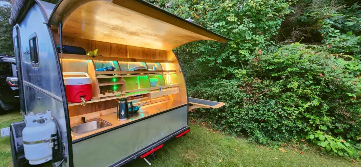RV rental: Teardrop trailer's illuminated outdoor kitchen with sink, cooler, and propane tank, ideal for camping.. Bend Teardrop Tall Boy 2023