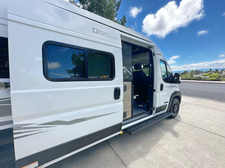 White National Park Foundation RV rental camper van with its side door open and step extended.. Winnebago Solis 2025