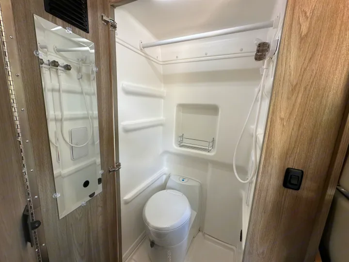 Inside an RV rental, this clean and compact bathroom includes a shower, toilet, and built-in storage for efficient use of space.. Winnebago Solis 2025