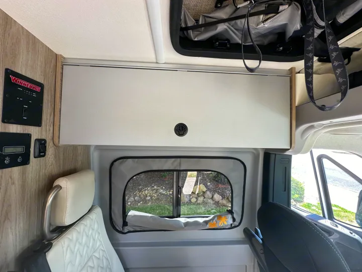 RV rental interior: A Winnebago camper van with light gray overhead storage, control panel, and a window shade featuring palm trees.. Winnebago Solis 2025