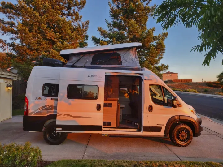 White Winnebago Solis camper van with raised pop-top roof and open side door showing interior, perfect for your next rv rental adventure.. Winnebago Solis 2025