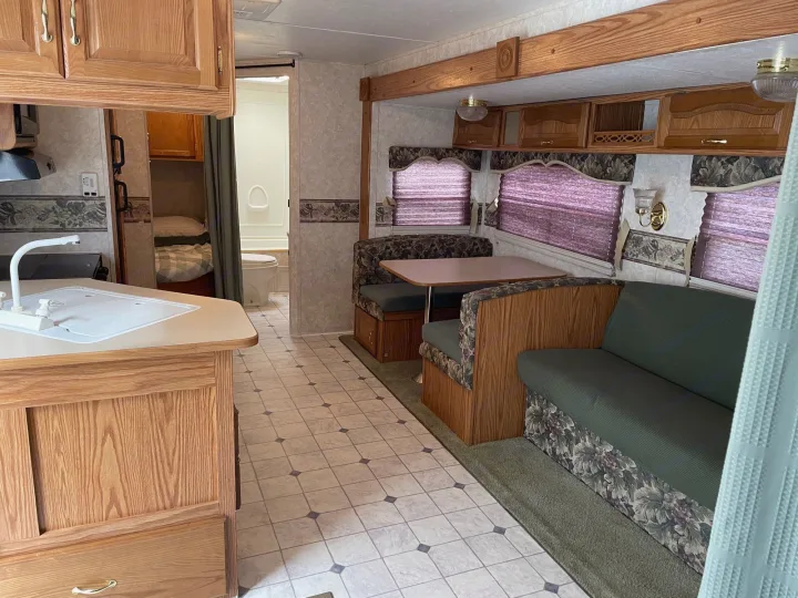 Spacious RV rental interior featuring a full kitchen, dining booth, and sofa, with a bedroom and bathroom visible.. Keystone RV Cougar 2003