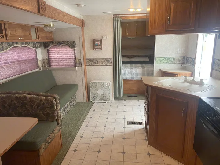 An rv rental interior featuring a cozy living area, a compact kitchen with a sink, and a bed behind a curtain.. Keystone RV Cougar 2003