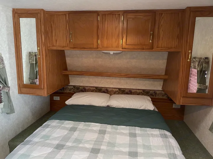 RV rental bedroom featuring wood overhead cabinets, mirrored doors, and a cozy plaid bed.. Keystone RV Cougar 2003