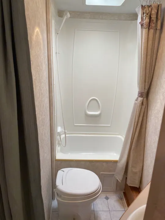 Compact RV rental bathroom with a white tub-shower, toilet in front, and patterned curtains. Essential for comfortable travel.. Keystone RV Cougar 2003