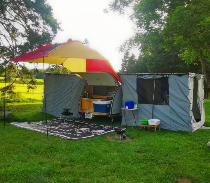 This RV rental teardrop trailer is fully set up for an outdoor camping adventure with an attached kitchen and tent.. Car-gotrailers liberty2goXL 2021