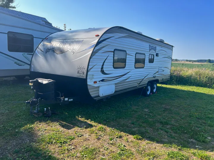 A Forest River Wildwood travel trailer, advertised for rv rental by Hill Top Rentals, sits in a sunny field.. Forest River Wildwood X-Lite 2017