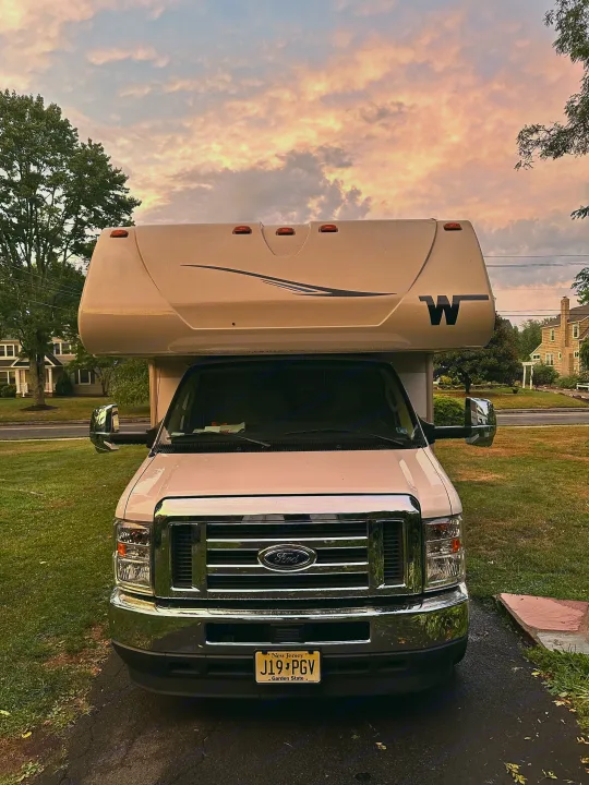 Front view of a white Class C RV rental, a Ford, parked on a New Jersey driveway under a picturesque evening sky.. Winnebago Minnie Winnie 2022