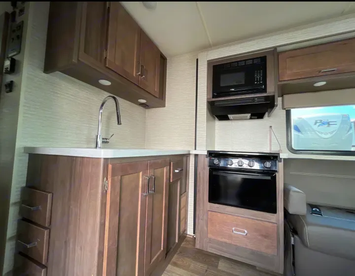 RV rental kitchen interior: modern sink, pull-down faucet, microwave, stove, oven, and ample wood cabinets.. Winnebago Minnie Winnie 2022