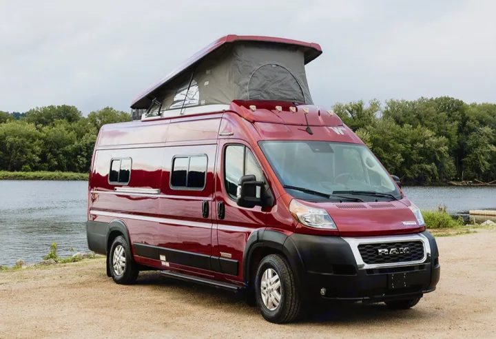 A striking red pop-top camper van parked by a river, ready for an exciting rv rental adventure.. Winnebago Solis 2023