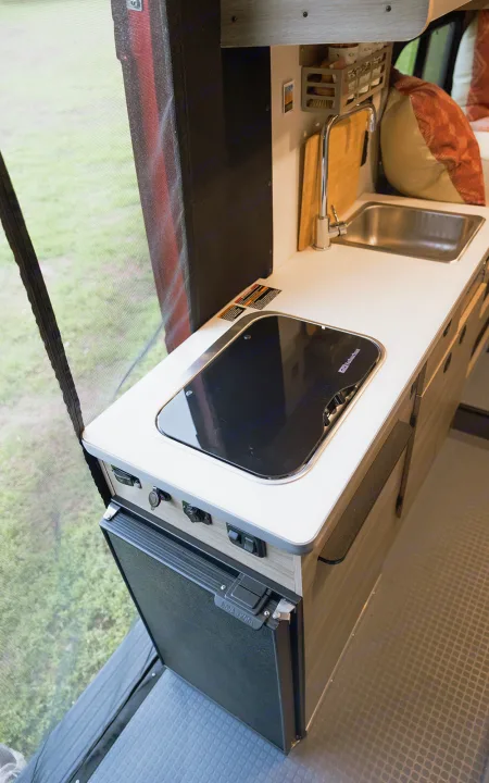Compact RV rental kitchen features Suburban stovetop, Nova Kool fridge, & sink for easy meal prep on the go.. Winnebago Solis 2023