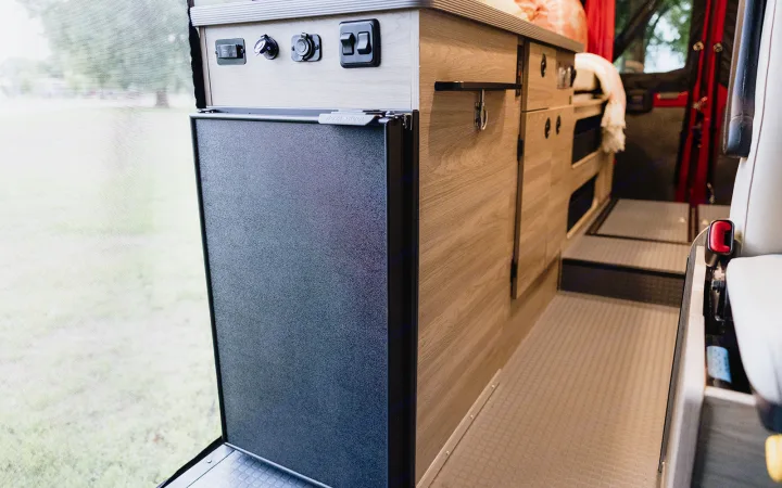 RV rental: Inside a camper van with a Nova Kool refrigerator, control panel, and wood storage cabinets.. Winnebago Solis 2023