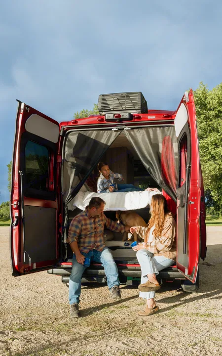 Inside an **rv rental**: A family and dog relax in their red camper van with open doors, enjoying the outdoors.. Winnebago Solis 2023