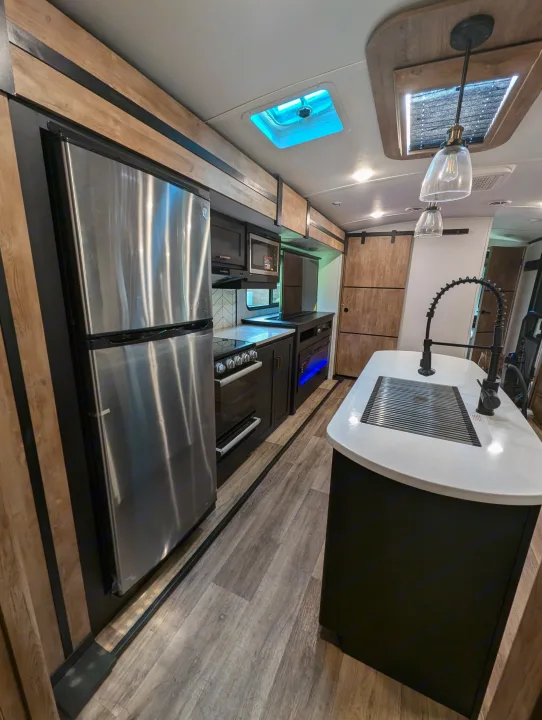 Modern RV kitchen interior: sleek design, stainless steel appliances, kitchen island with sink. Ideal for an RV rental journey.. Keystone RV Outback 2022