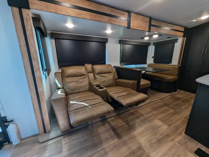Spacious RV rental interior featuring comfy recliners, a dinette, and modern wood-accented design, ideal for travel.. Keystone RV Outback 2022