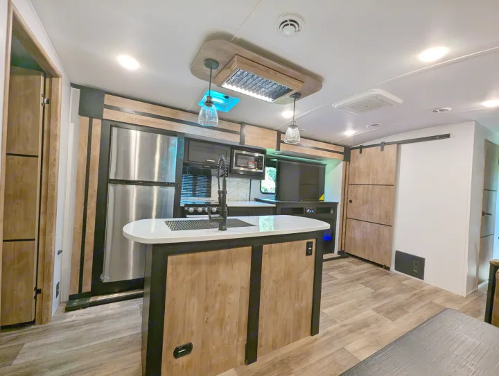 Inside a modern RV rental: a bright kitchen with island, stainless appliances, wood-look finishes, and contemporary design.. Keystone RV Outback 2022