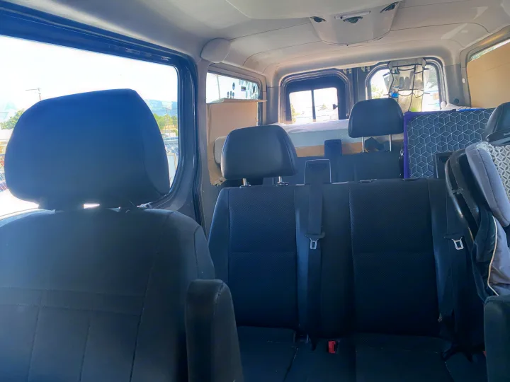 Cozy RV rental interior: view from front seats showing spacious rear seating and a neatly set up bed area.. Mercedes Sprinter 2011