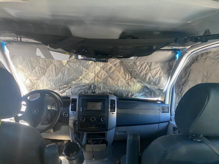 Cozy rv rental interior with quilted windshield covers for privacy and insulation. Overhead net storage and detailed dashboard visible.. Mercedes Sprinter 2011