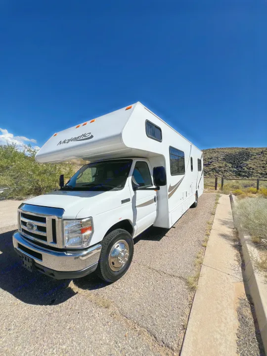 A large, white Majestic Class C RV rental, featuring a Ford grille, is parked on a gravel lot under clear blue skies.. Thor Majestic 2019