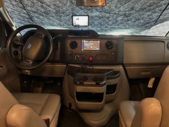 RV rental interior: Ford E-Series van dashboard, steering wheel, and infotainment screen with a quilted windshield sunshade.. Thor Majestic 2019