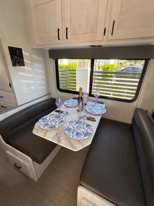 An inviting RV rental dining nook with patterned plates, purple glasses, and a champagne bottle, perfect for a cozy trip.. Entrada East to West 2024