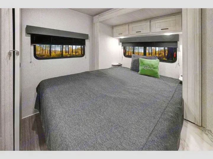 Comfortable RV rental bedroom featuring a cozy bed, overhead cabinets, and scenic nature views from the windows.. Entrada East to West 2024