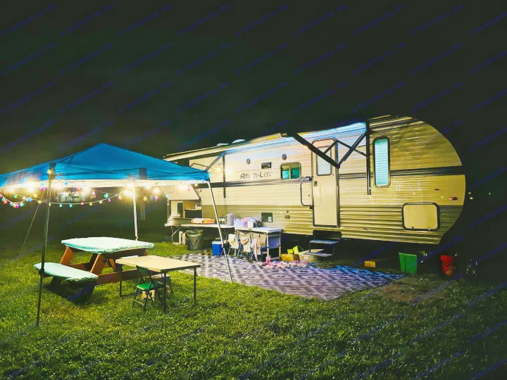 Enjoying an RV rental setup at night: travel trailer with lighted awning, outdoor kitchen, picnic area under a lit canopy.. Gulf Stream Ameri-Lite 2021