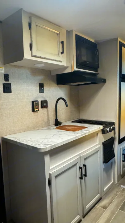 Functional RV rental kitchen: white countertop, black sink & faucet, microwave, stovetop, and light-toned cabinets.. Jayco Jay Flight SLX 2022