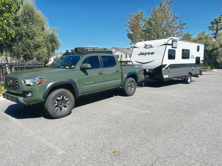 A green Toyota Tacoma pickup truck tows a Jayco travel trailer RV rental, parked on asphalt under clear skies.. Jayco Jay Flight SLX 2022