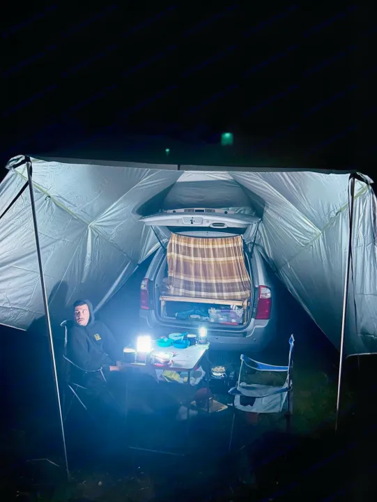 Nighttime car camping offers comfort like an rv rental. Cozy setup under a lit tent attached to the vehicle.. KIA SEDONNA 2008