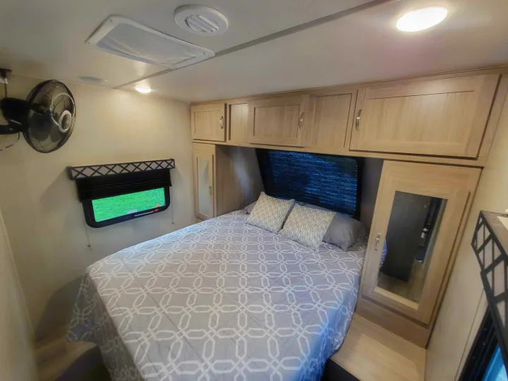 Comfortable RV rental bedroom featuring a queen bed, overhead cabinets, wall fan, and window. Perfect for your travels.. Coachmen Freedom Express 248RBS 2020