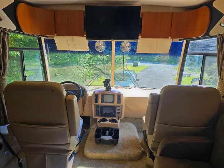Interior view of an RV rental showing the cockpit, dashboard, and front seats with a windshield view of the road.. Winnebago Sightseer 2008