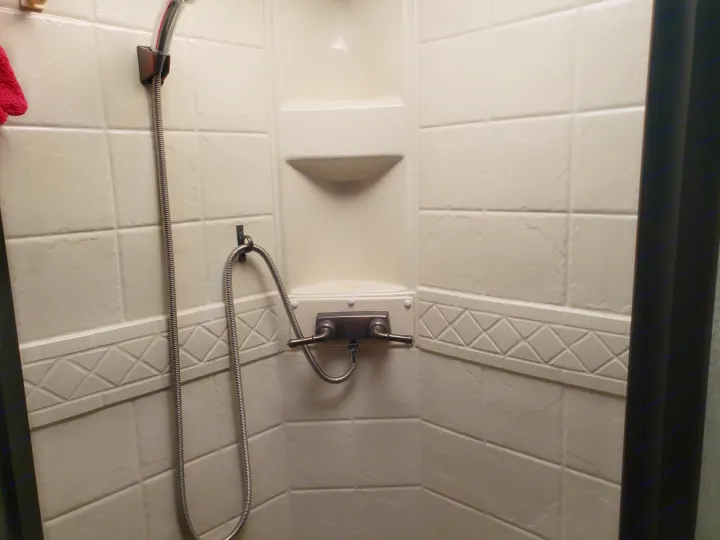 An RV rental shower featuring beige tiled walls, a handheld showerhead, and classic faucet controls for a comfortable wash.. Four Winds Freedom Elite 2010