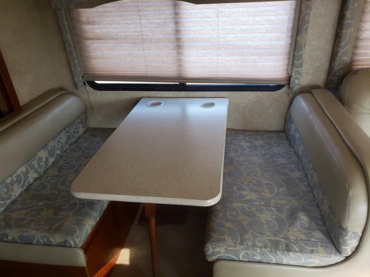 RV rental dinette featuring a light-colored table with cup holders, flanked by patterned upholstered bench seats.. Four Winds Freedom Elite 2010