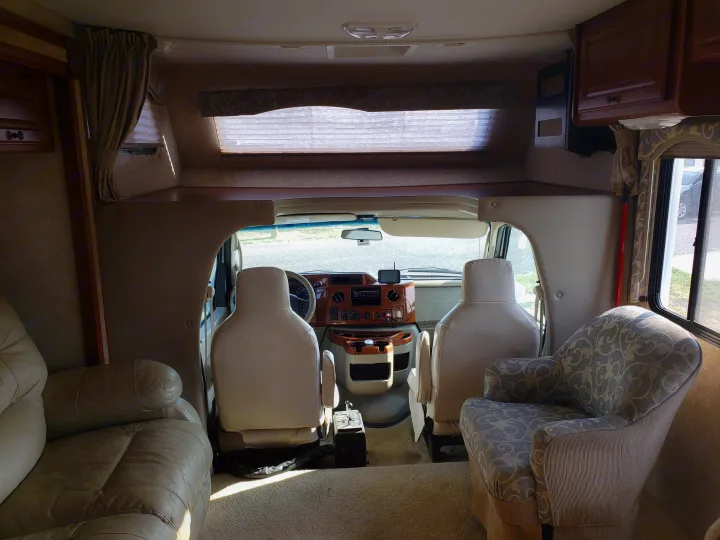 RV rental interior: view from the living area towards the cockpit, featuring cream seats, dashboard, leather sofa, and patterned armchair.. Four Winds Freedom Elite 2010