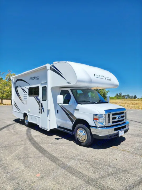 This white "Freedom Elite" Class C RV rental is parked on asphalt under a clear blue sky, ready for your next adventure.. Thor Freedom Elite 2019