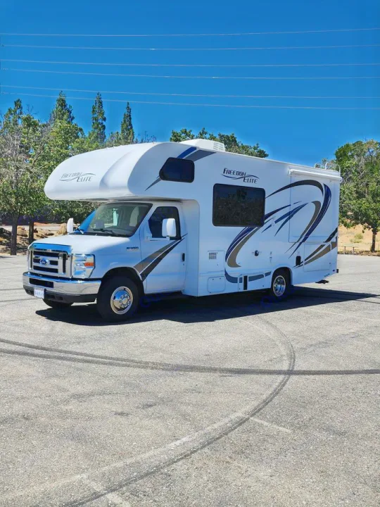 Bright white Class C RV rental, "Freedom Elite" branded, parked on an asphalt lot with tire marks.. Thor Freedom Elite 2019