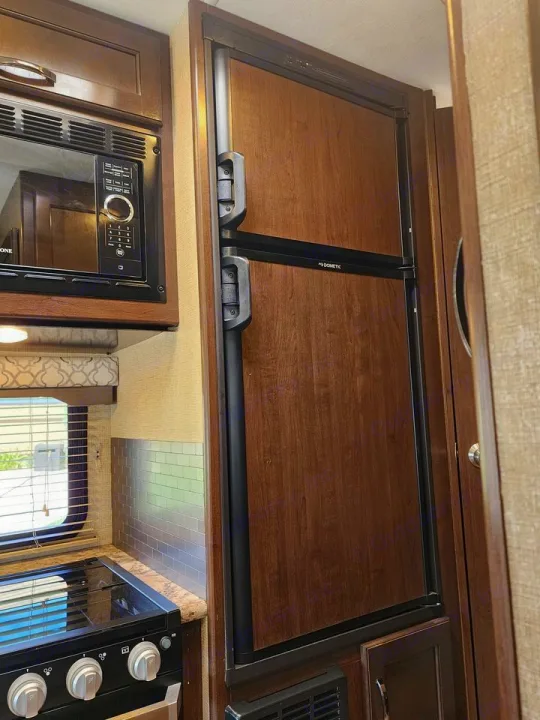 RV rental's compact kitchen featuring a Dometic refrigerator, microwave, and stovetop for travel comfort.. Thor Freedom Elite 2019