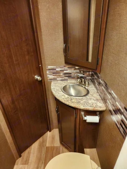 Compact RV rental bathroom with corner sink vanity, medicine cabinet, toilet, and a stylish tiled backsplash.. Thor Freedom Elite 2019