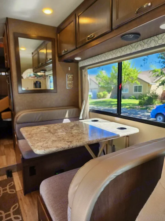 RV rental interior: cozy dinette with a table and benches, overhead cabinets, and a clear window view outside.. Thor Freedom Elite 2019