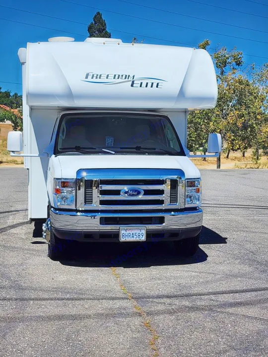 Front view of a white Freedom Elite RV rental, a Ford Class C motorhome, parked on asphalt. California plate 8HRA589.. Thor Freedom Elite 2019