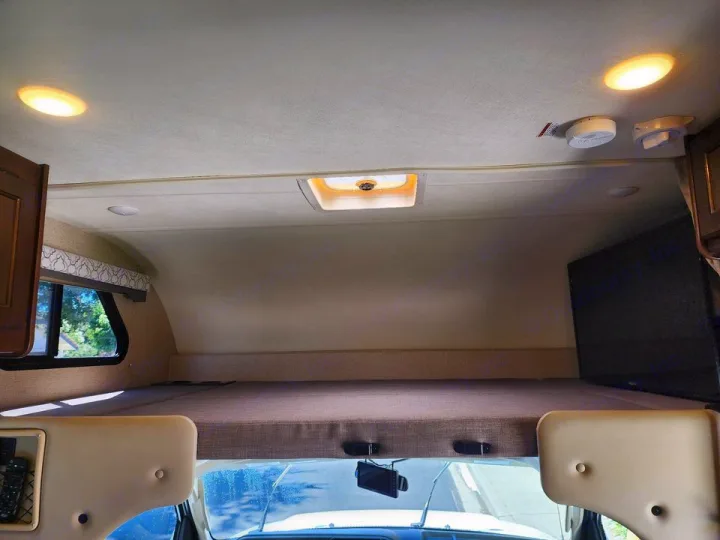 Inside an **RV rental**: cozy overhead bunk bed, ceiling lights, vent, window, and TV. Perfect for adventurous travel!. Thor Freedom Elite 2019