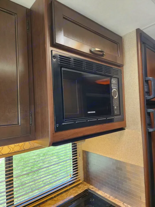 RV rental kitchen: microwave, wood cabinets, window blinds, and metallic backsplash.. Thor Freedom Elite 2019