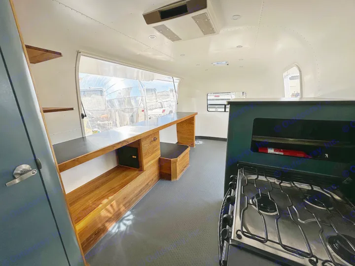 Spacious Airstream RV rental interior: kitchen with stove, wood counter, and large window view of other trailers.. Airstream Custom 2006