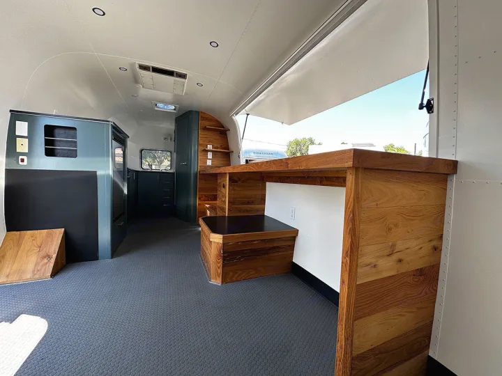 Spacious custom Airstream RV rental with modern wood and teal cabinetry, featuring a large serving window.. Airstream Custom 2006