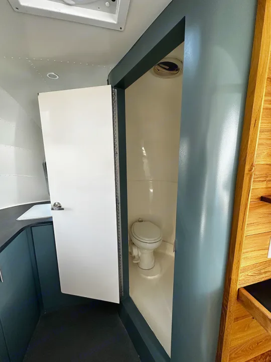 An RV rental's compact bathroom features a toilet in a light-colored enclosure, with the door open to a sink area.. Airstream Custom 2006