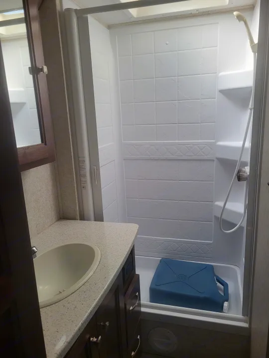 Compact RV rental bathroom with a vanity, sink, and shower stall, featuring a blue water jug inside the shower.. Forester Forester Motorhome 2020
