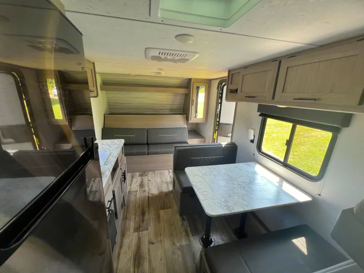 Interior of an rv rental, showing a kitchen on the left, a dinette, and a sofa bed. Bright window on right illuminates the modern camper.. Coleman Lantern 18 2024
