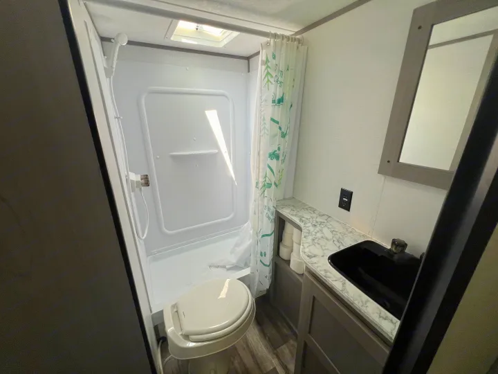 Compact RV rental bathroom featuring a shower with a toilet inside, vanity with a black sink, and mirror.. Coleman Lantern 18 2024